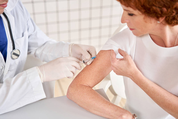 Male doctor holding syringe making covid 19 vaccination injection dose in shoulder of female patient. Corona virus vaccine clinical trials concept . - Фото, зображення