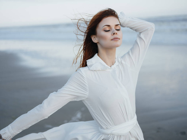 A woman in a white dress walks along the ocean shore  - 写真・画像