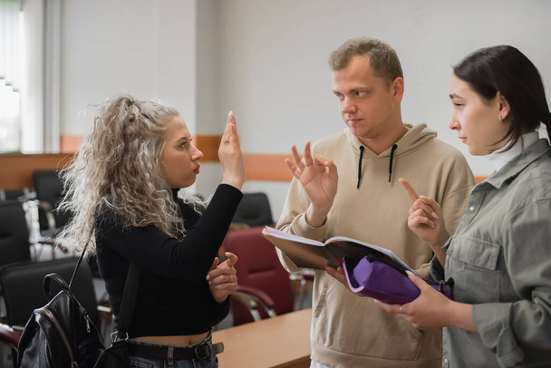 Two girls and a guy are talking in sign language. Three deaf students chatting in a university classroom. - Valokuva, kuva