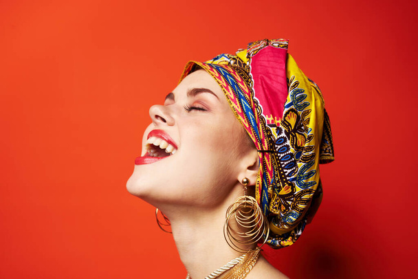όμορφη γυναίκα εθνικότητα πολύχρωμη μαντίλα μακιγιάζ αίγλη κόκκινο φόντο - Φωτογραφία, εικόνα