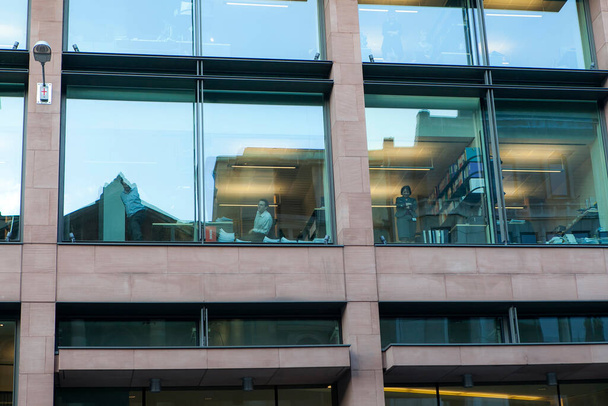 LONDON, ENGLAND - NOVEMBER 19 2017: Students take part in a protest march against fees and cuts in the education system . People in an office building look out the window at the street - Foto, immagini