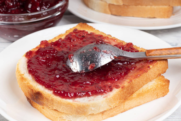 Vista de cerca de Raspberry Jam con pan tostado en mesa blanca. Enfoque selectivo. - Foto, Imagen