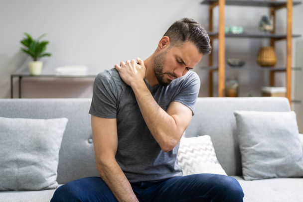 Mann mit Schulterschmerzen auf Couch zu Hause - Foto, Bild