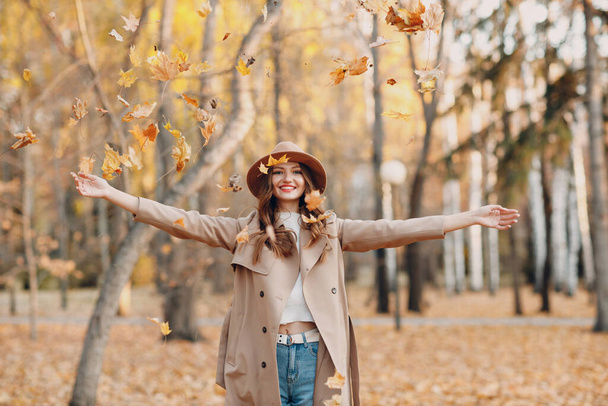 黄色の葉を持つ秋の公園の若い女性モデルカエデの葉。秋のファッション. - 写真・画像