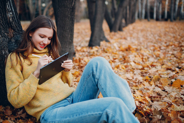 MOSKAU, RUSSLAND - 19. OKTOBER 2021: Junge Frau sitzt mit Tablet Apple iPad Pro 2021 und malt mit Bleistift im Herbstpark - Foto, Bild