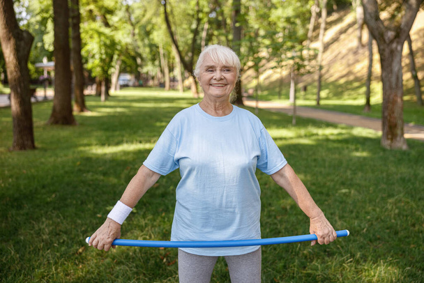 Cheerful mature woman holds plastic bar standing in green park - 写真・画像