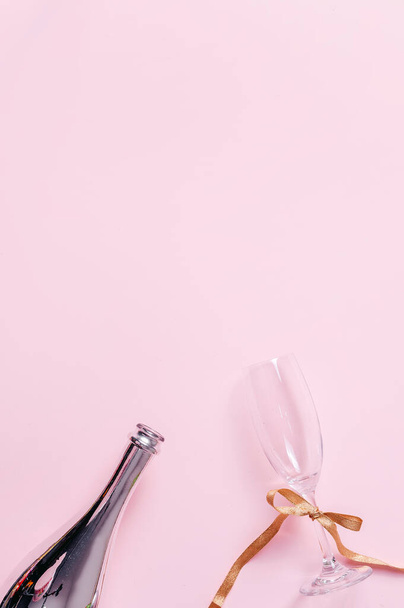 Glass of champagne and silver champagne bottle on pink paper background minimal style holiday background. - Photo, Image