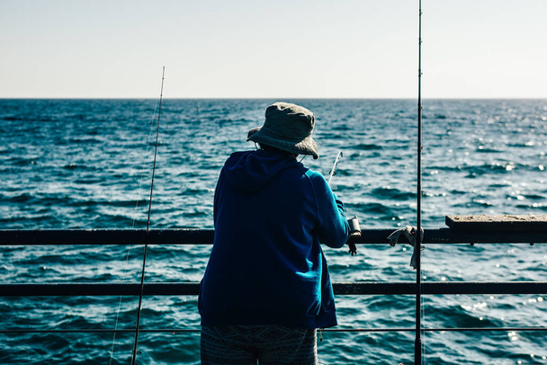 A rear view of a fisher on the boat with a fishing rod in the open sea on a sunny day - Photo, Image