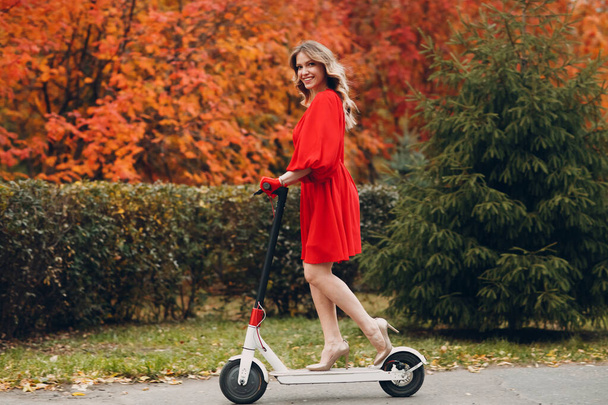 Sonbahar şehrinde elektrikli scooter kullanan genç bir kadın. - Fotoğraf, Görsel