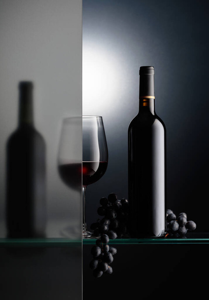 Butelki i kieliszek czerwonego wina z bandą niebieskich winogron. Martwa natura jest częściowo pokryta mrożoną szklanką. Przestrzeń kopiowania.  - Zdjęcie, obraz