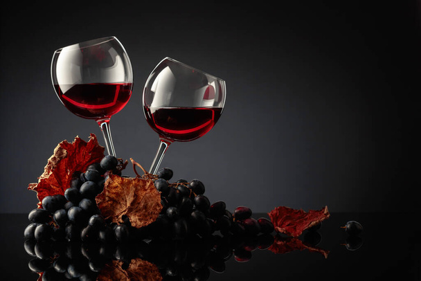 Bril rode wijn en blauwe druiven op een zwarte achtergrond. Kopieerruimte. - Foto, afbeelding