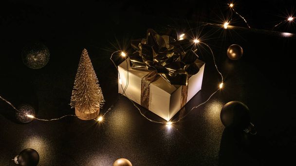 ホリデークリスマスの背景。金色のリボン、新年のボールと輝くライトが付いた白いギフトボックスは、グリーティングカードのための黒のxmas組成でガーランド。冬休み、新年 - 写真・画像