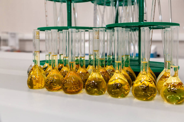 Chiudere una lunga fila di fiaschette di vetro con una soluzione gialla su un banco da laboratorio
 - Foto, immagini