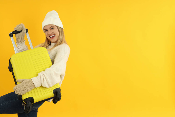 Aantrekkelijk meisje in de winter kleding met bagage tas op gele achtergrond. - Foto, afbeelding