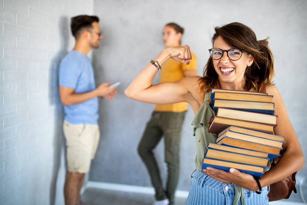 Genießen Sie das Universitätsleben. Schöne glückliche Frau hält Bücher in der Hand und lächelt mit seinen Freunden, die im Hintergrund plaudern - Foto, Bild