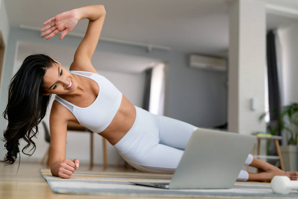 Young fit woman in sportswear watching online video with fitness exercises on laptop at home - Photo, image