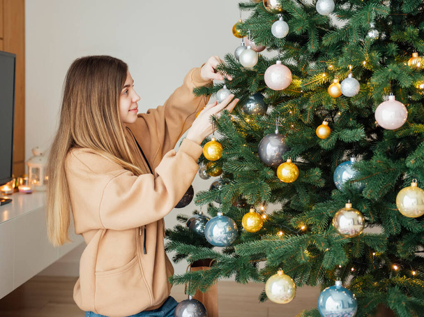 Tinédzser lány díszíti a karácsonyfát. Karácsonyfa a nappaliban. - Fotó, kép