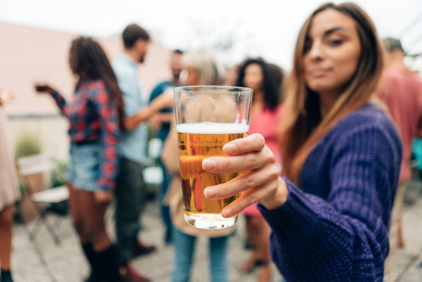 weibliche Hand hält Bier auf der Party - Mädchen bietet Drink oder Prost mit einem Pint auf dem Dachfest - Foto, Bild
