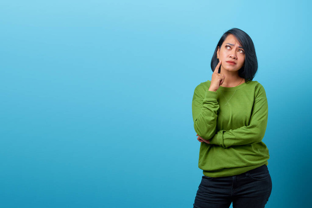 Attractive Asian woman thinking and looking up empty space on blue background - Foto, Imagem