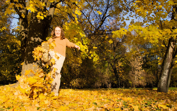 Дефокусована молода смішна жінка вбиває сухе осіннє листя ногою в лісі в сонячний день. Щастя
. - Фото, зображення