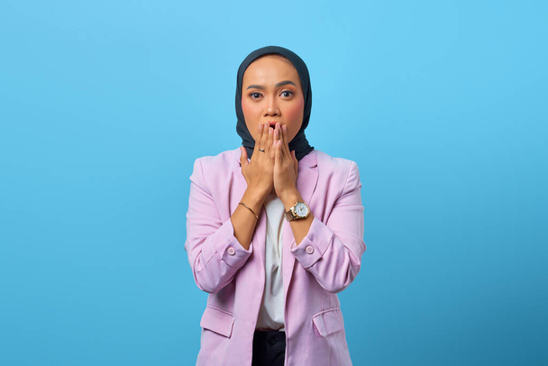 Surprised Asian woman covering mouth with hands over blue background - Φωτογραφία, εικόνα