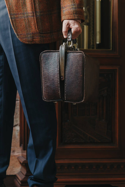 vintage leather bag in the left hand of a man in strict blue trouser - Foto, imagen