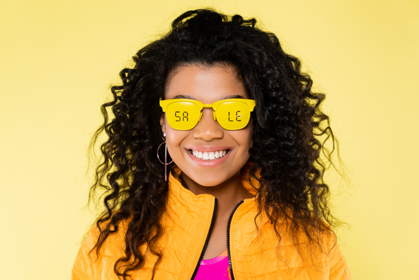 улыбающаяся африканская молодая женщина в солнцезащитных очках с надписью на желтом - Фото, изображение