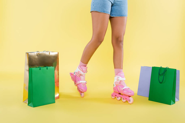 cropped view of african american woman in roller skates near shopping bags on yellow - Foto, Imagem