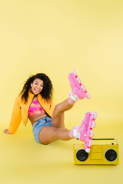 comprimento total de mulher americana africana animado em patins sentados perto boombox retro no amarelo - Foto, Imagem