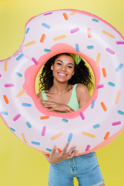 feliz afro-americana jovem segurando anel inflável isolado no amarelo - Foto, Imagem