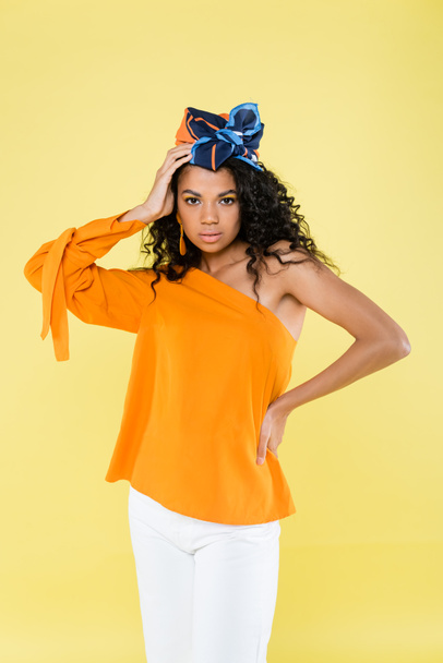 curly african american woman in headscarf and bare shoulder posing with hand on hip isolated on yellow - Foto, immagini