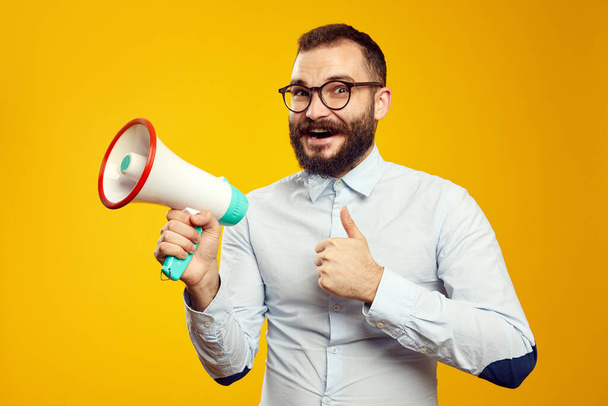 Man holding megaphone and smiling while showing thumb up over yellow backdrop - 写真・画像
