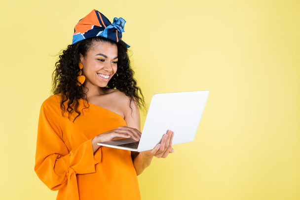 smiling african american woman using laptop isolated on yellow - Foto, Imagen
