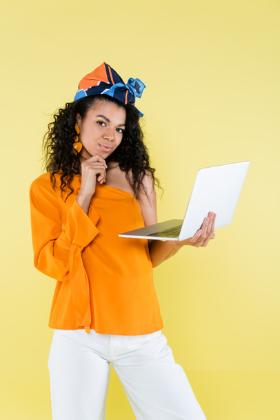 nachdenkliche Afroamerikanerin mit Laptop isoliert auf gelb - Foto, Bild