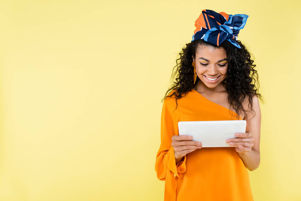 sonriente mujer afroamericana sosteniendo tableta digital aislada en amarillo - Foto, imagen