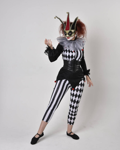 Full length  portrait of red haired  girl wearing a black and white clown jester costume, theatrical circus character.  Standing pose  isolated on  studio background. - Photo, Image