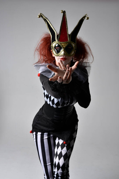 close up portrait of red haired  girl wearing a black and white clown jester costume, theatrical circus character.  Standing pose  isolated on  studio background. - Photo, Image