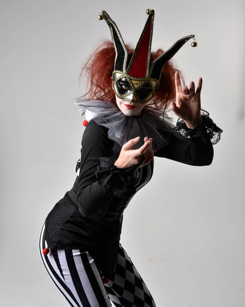 Nahaufnahme Porträt eines rothaarigen Mädchens in einem schwarz-weißen Clownskostüm, theatralischer Zirkusfigur. Stehende Pose isoliert auf Studiohintergrund. - Foto, Bild