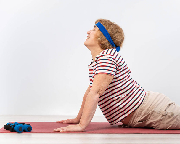 Elderly woman doing exercises in the studio on a white background. The old lady is doing fitness for health - Foto, Bild
