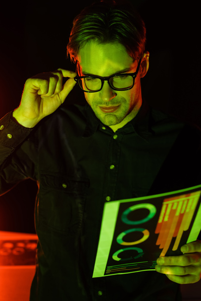 Programista trzymający okulary i dokumenty z wykresami odizolowanymi na czarno  - Zdjęcie, obraz