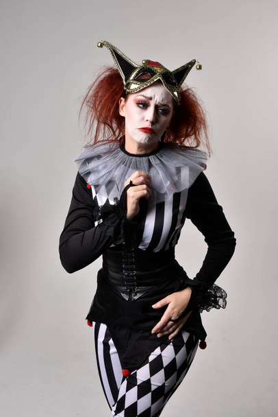 close up portrait of red haired  girl wearing a black and white clown jester costume, theatrical circus character.  Standing pose  isolated on  studio background. - Фото, зображення