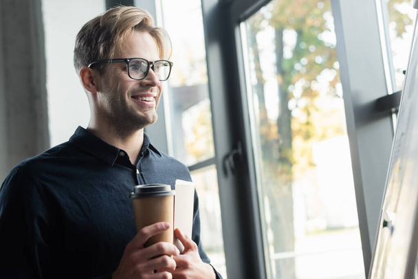 Счастливый программист с кофе и бумажной папкой, стоящей возле флип-чарта в офисе  - Фото, изображение