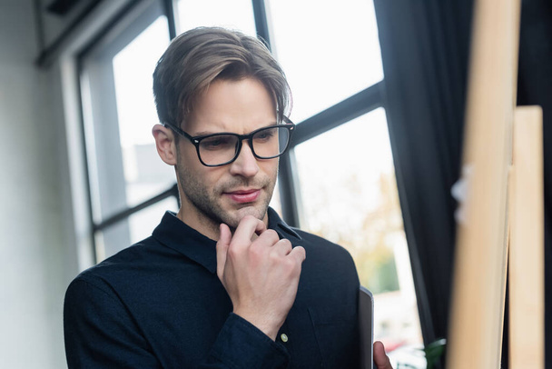 Pensive programmer in eyeglasses looking at flip chart in office  - Zdjęcie, obraz