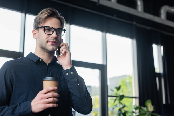 Programmer talking on mobile phone and holding paper cup in office  - Foto, immagini