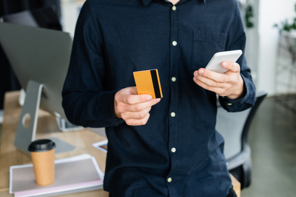 Cropped view of programmer using smartphone and credit card in office  - Photo, image