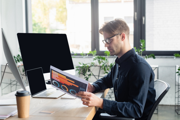 Вид сбоку программиста, работающего с бумагой у компьютеров и кофе в офисе  - Фото, изображение