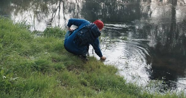 Retkeilijä, jolla on reppu juo vettä tuntemattomasta joesta - Valokuva, kuva