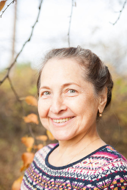 Портрет красивой пожилой женщины в свитере на фоне осеннего пейзажа.  - Фото, изображение