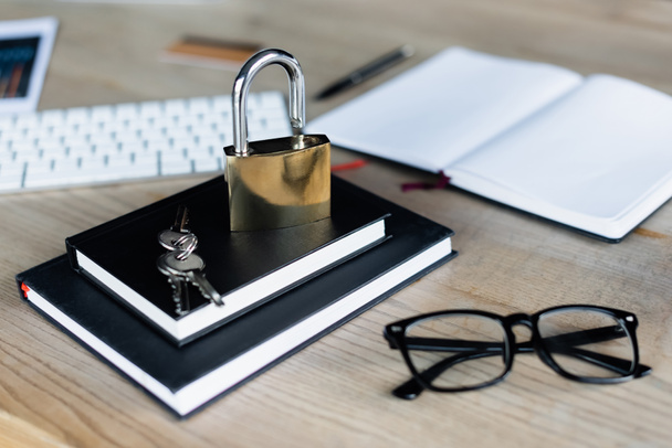 Padlock and keys on notebooks near eyeglasses and keyboard in office  - Foto, immagini