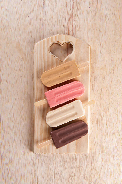 Various popsicles are placed on the wooden board background. Caramel, strawberry, vanilla and chocolate flavor. Top view. Copy sapce - Photo, Image